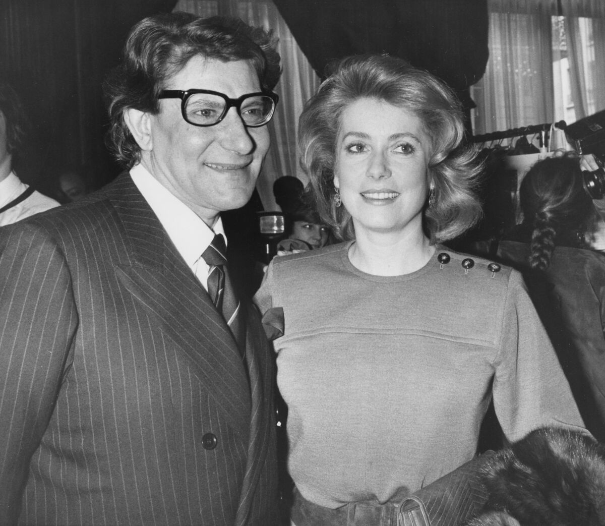 FILE - In this Jan. 30 1985 file photo, French actress Catherine Deneuve congratulates French fashion designer Yves Saint Laurent after the presentation of spring-summer haute couture collection in Paris. Denueve's family said in a statement released Wednesday Nov. 6, 2019, that the 76-year-old actress suffered a "very limited and therefore reversible" stroke. (AP Photo/Alexis Duclos, File)