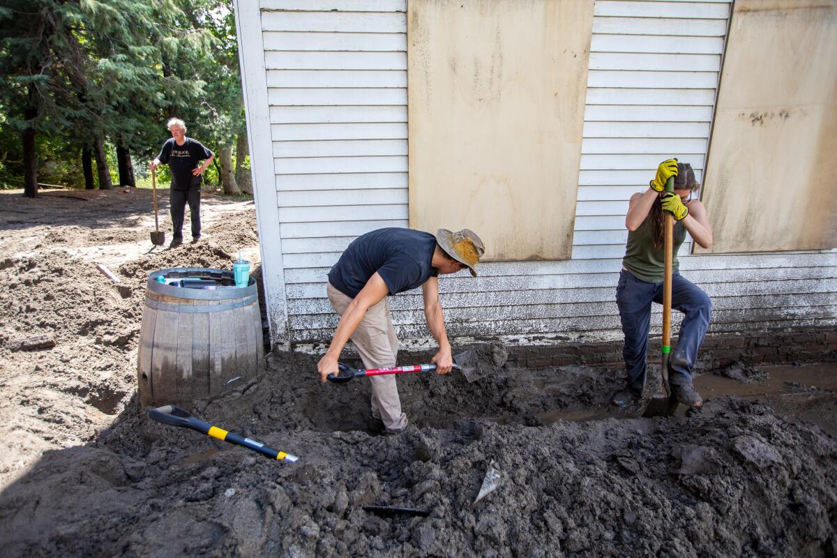Workers shovel mud near the foundation of a building.