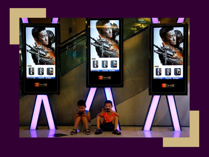 Children use smartphones near monitors displaying a Chinese action movie "Wolf Warrior 2" at a cinema in Beijing.