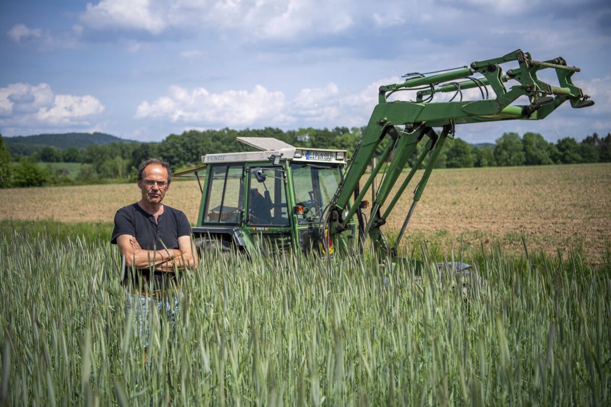 Ulf Allhoff-Cramer, farmer, stands in a rye field in front of his tractor in Detmold, Germany, Wedenesday, May 18, 2022. The organic farmer holds the VW car company partly responsible for damage to his farm. Together with Greenpeace, he wants to go to court to get VW to stop producing combustion vehicles by 2030. (Lino Mirgeler/dpa via AP)