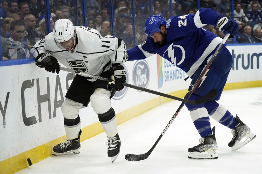 Los Angeles Kings center Anze Kopitar (11) and Tampa Bay Lightning defenseman Zach Bogosian (24) battle for the puck against the dasher during the first period of an NHL hockey game Tuesday, Dec. 14, 2021, in Tampa, Fla. (AP Photo/Chris O'Meara)
