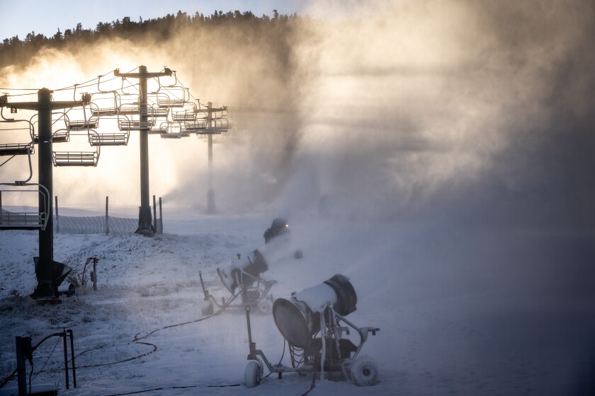 The sun lights up chairlifts as, in the shadow, snow blasts from machines.