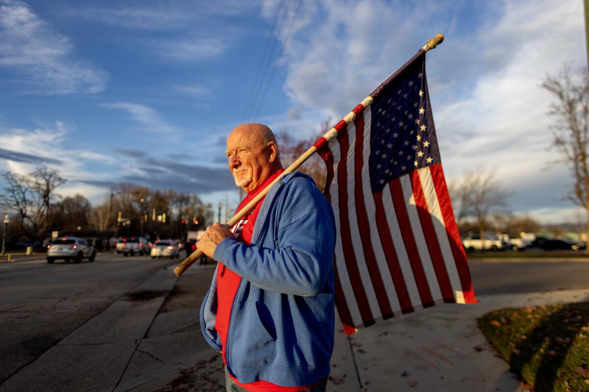 A man holds an American flag while campaigning on a street corner