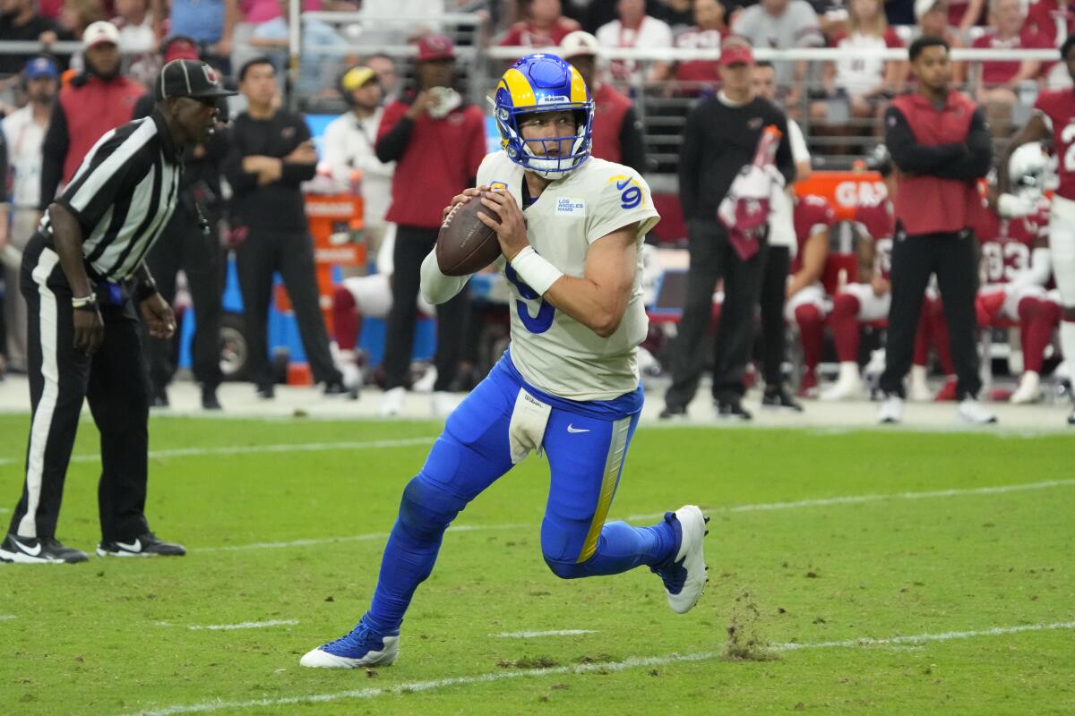 Rams quarterback Matthew Stafford looks to pass the football while running on a field.