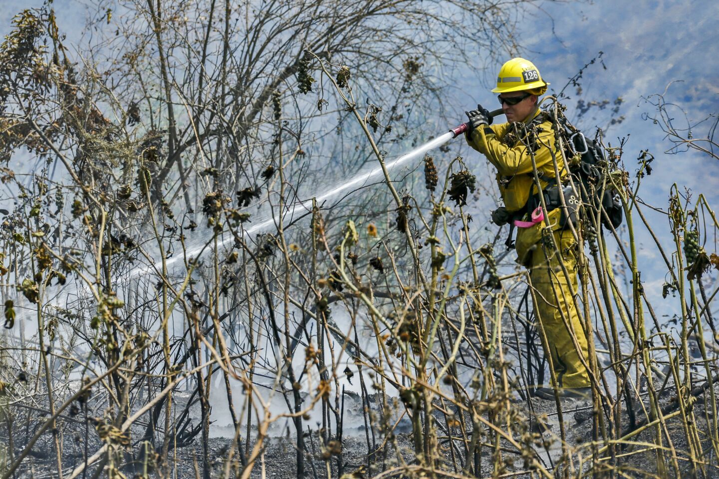 An LA County firefighter mops up hotspots on the hillside along 3200 block of Brookridge Rd. on Tuesday in Duarte.