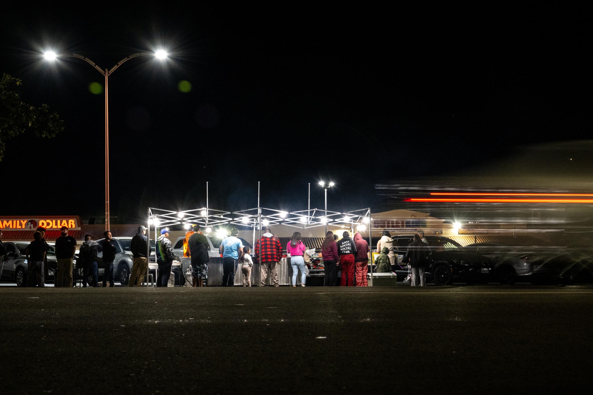 A crowd forms at a taco stand at night.