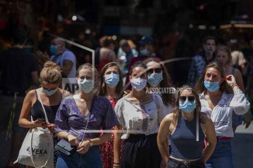 Tourists wearing face masks wait to cross a road in downtown Barcelona, Spain, Thursday, July 16, 2020. With Europe's summer vacation season kicking into high gear for millions weary of months of lockdown, scenes of drunken British and German tourists on Spain's Mallorca island ignoring social distancing rules and reports of American visitors flouting quarantine measures in Ireland are raising fears of a resurgence of infections in countries that have battled for months to flatten the COVID-19 curve. (AP Photo/Emilio Morenatti)