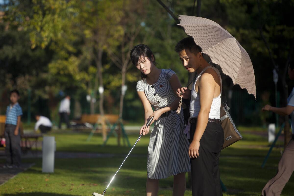 In this Sept. 8, 2012, photo, a man holds a woman's bag and parasol as they play miniature golf at a newly built amusement park in Pyongyang, North Korea.