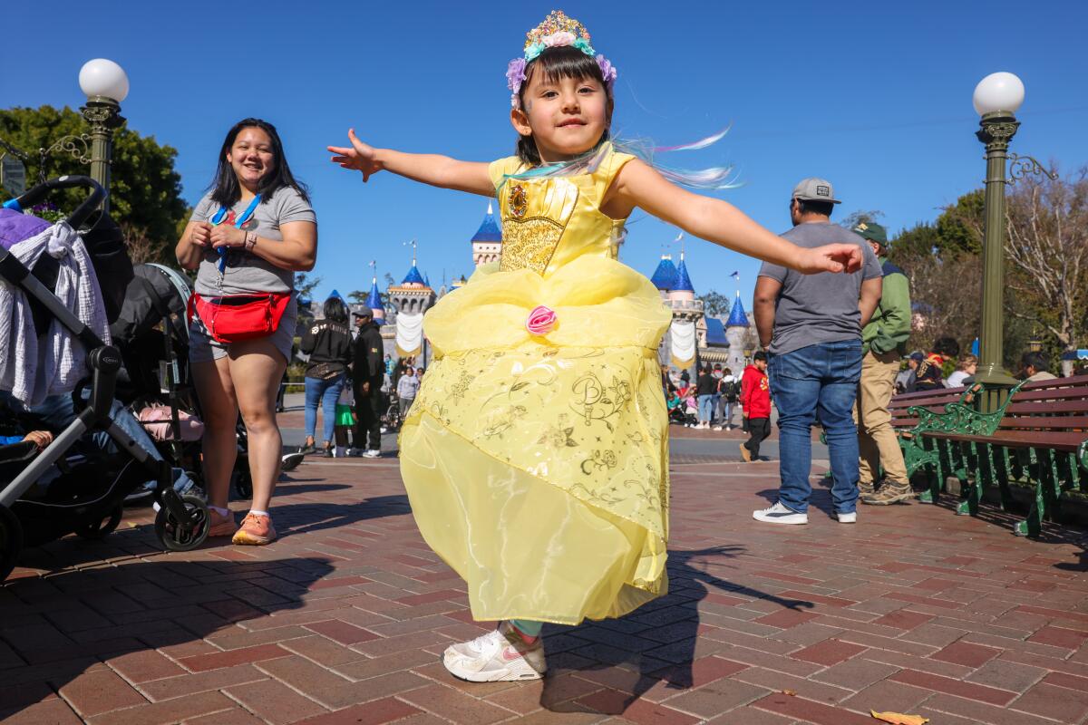 Una niña de 6 años gira con un vestido amarillo pálido. "Beldad" ropa en Disneylandia.