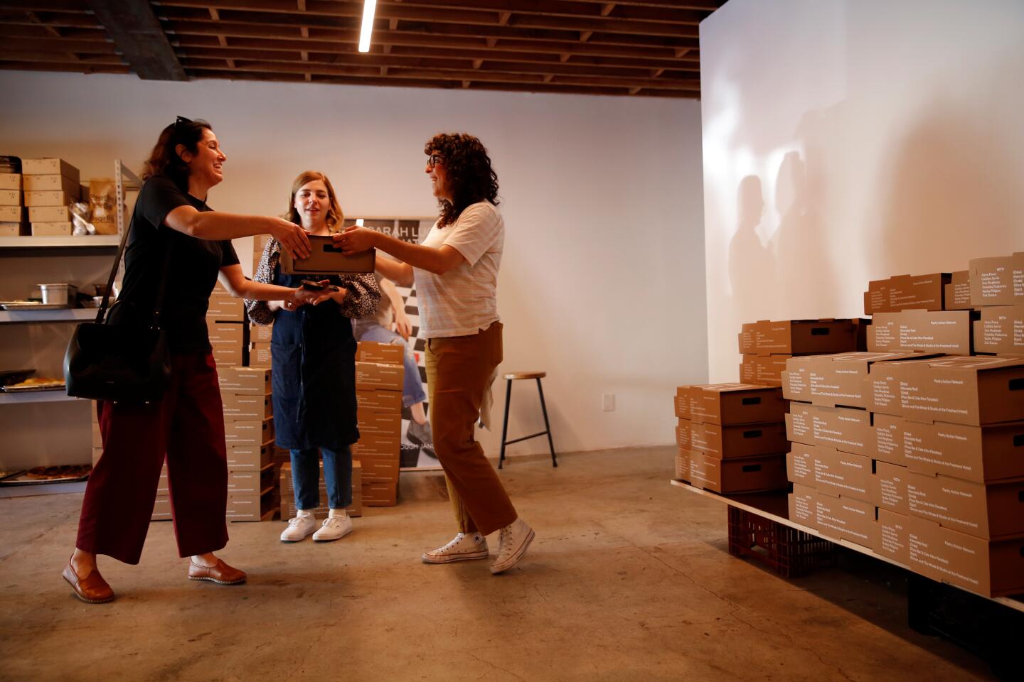Lillian Anjarjolian, left, receives a box of baked goods from chef Sasha Piligian as chef Anna Posey looks on at the Pastry Action Network's fundraiser.