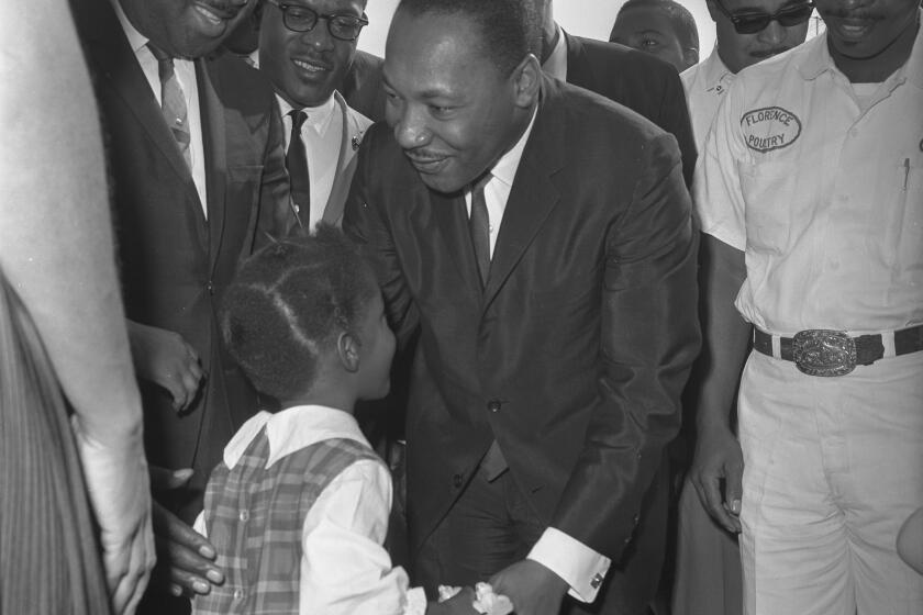 Dr. Martin Luther King Jr. smiles and bends toward a small girl in a plaid dress.