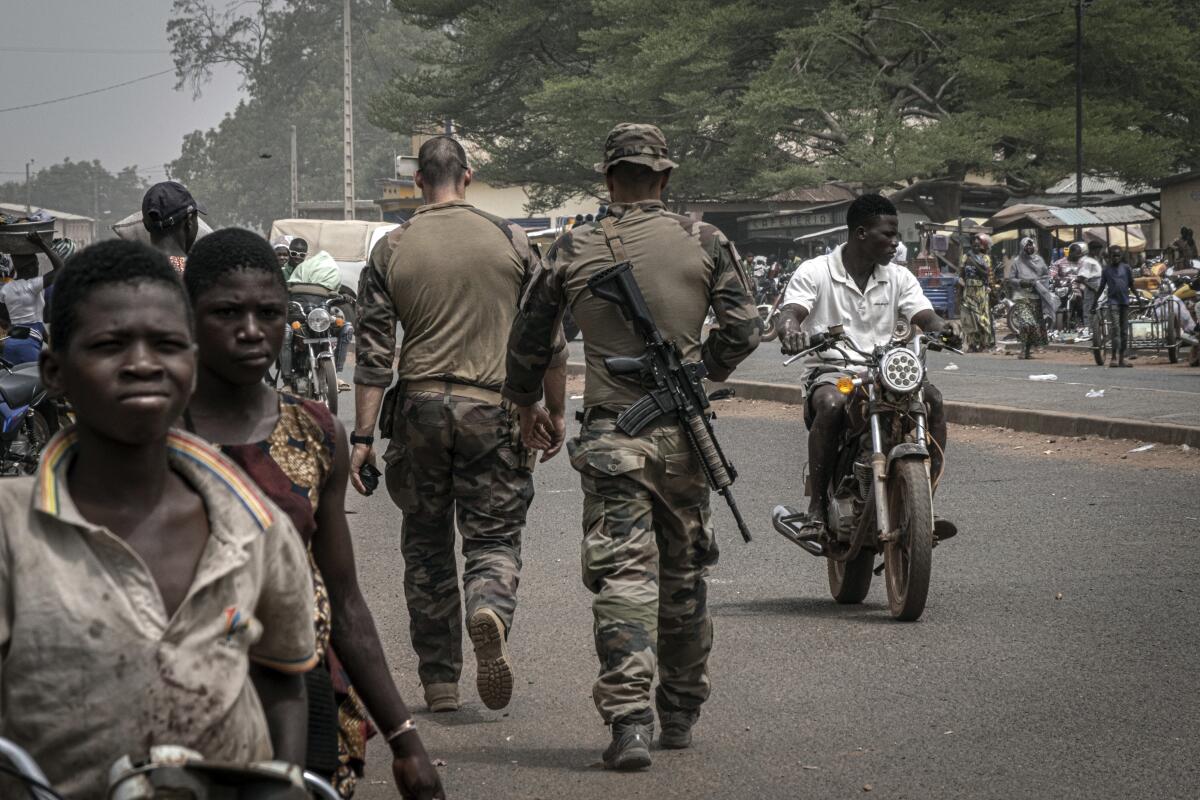 People in military gear walk a Benin street.