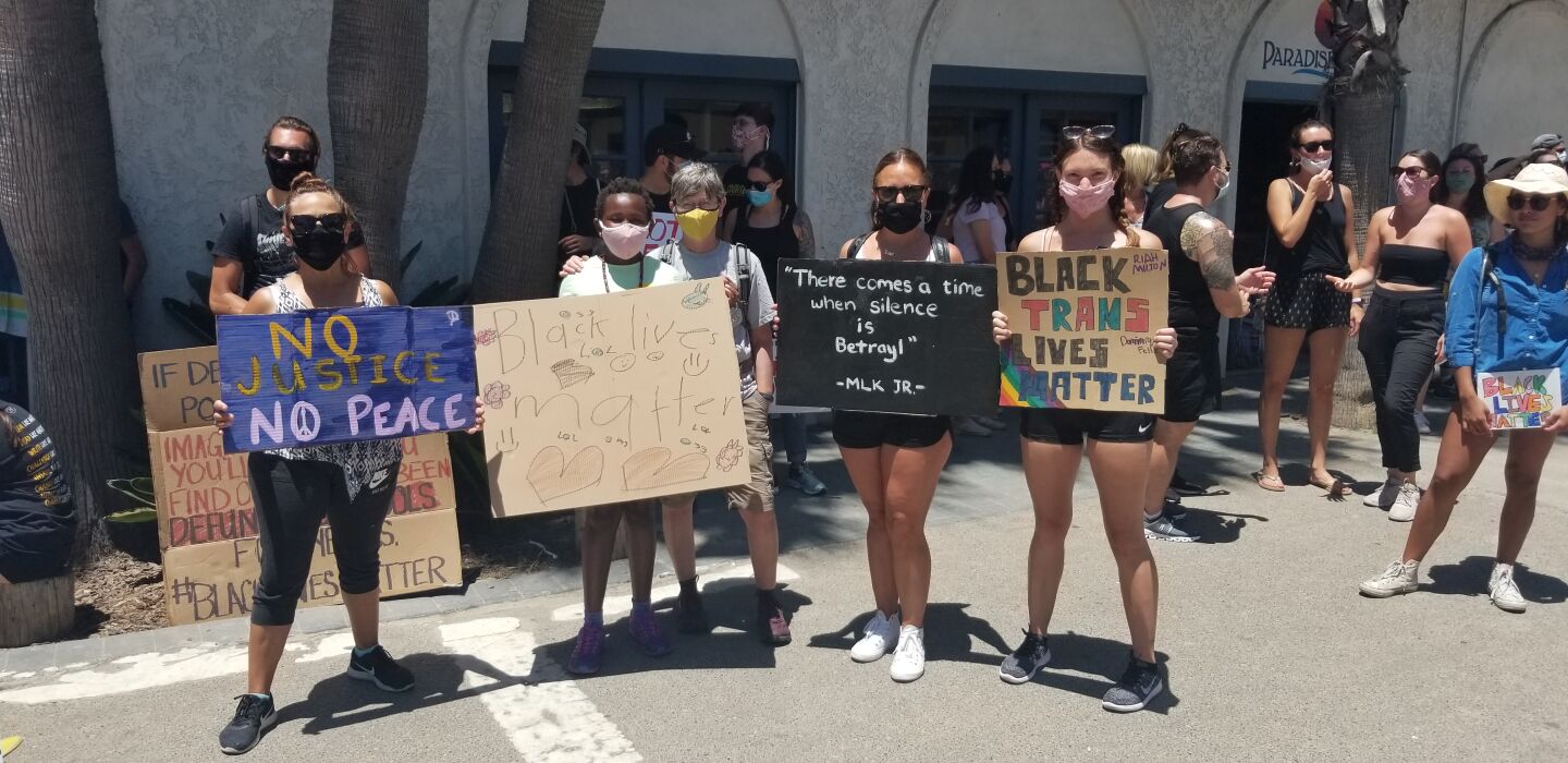 Community members stand with protest signs before the Pacific Beach Walk for Equality.