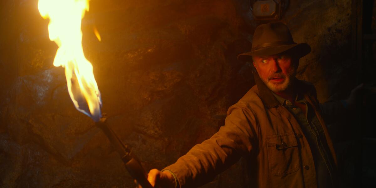 A man in a hat holding a torch in a dark cave