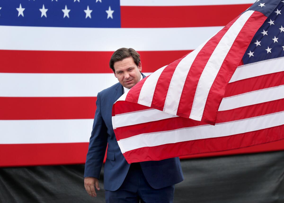 A man in a suit walks behind an American flag