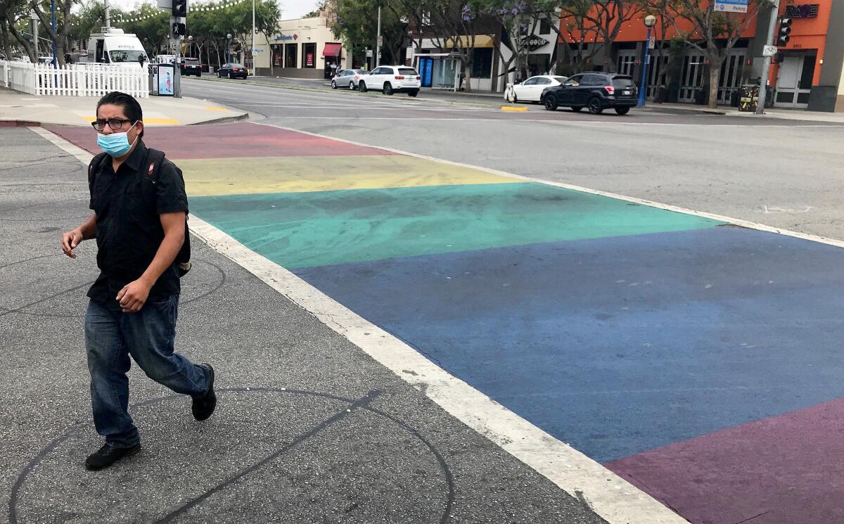 A man wearing a face covering crosses San Vicente Blvd. at Santa Monica Blvd. in West Hollywood