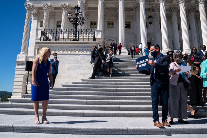 A woman exchanging words with a man on the U.S. Capitol steps as he shows her a sign reading, "Build back better for women."