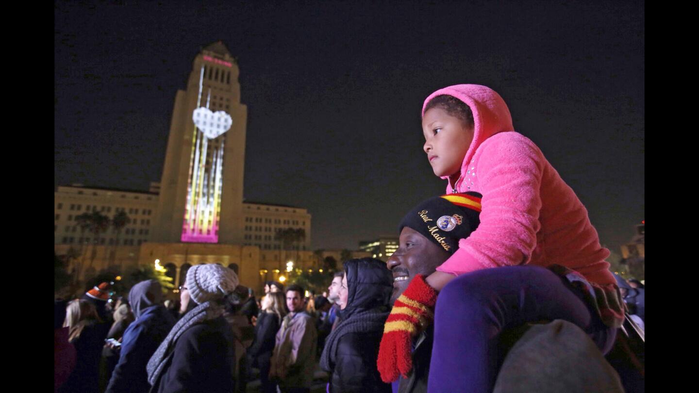 Sarah Doumbia, 4, sits on the shoulders of her father, Iba Doumbia, at Grand Park as lights are projected on City Hall during the New Year's Eve celebration on Wednesday night.