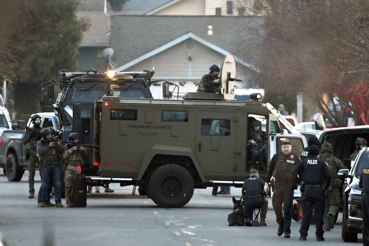 Law enforcement officers aim their weapons at a home during a standoff in Grants Pass, Ore., on Tuesday, Jan. 31, 2023. Police said the standoff involving a man suspected in a violent kidnapping in Oregon who was barricaded underneath the home has been “resolved.” (Scott Stoddard/Grants Pass Daily Courier via AP)
