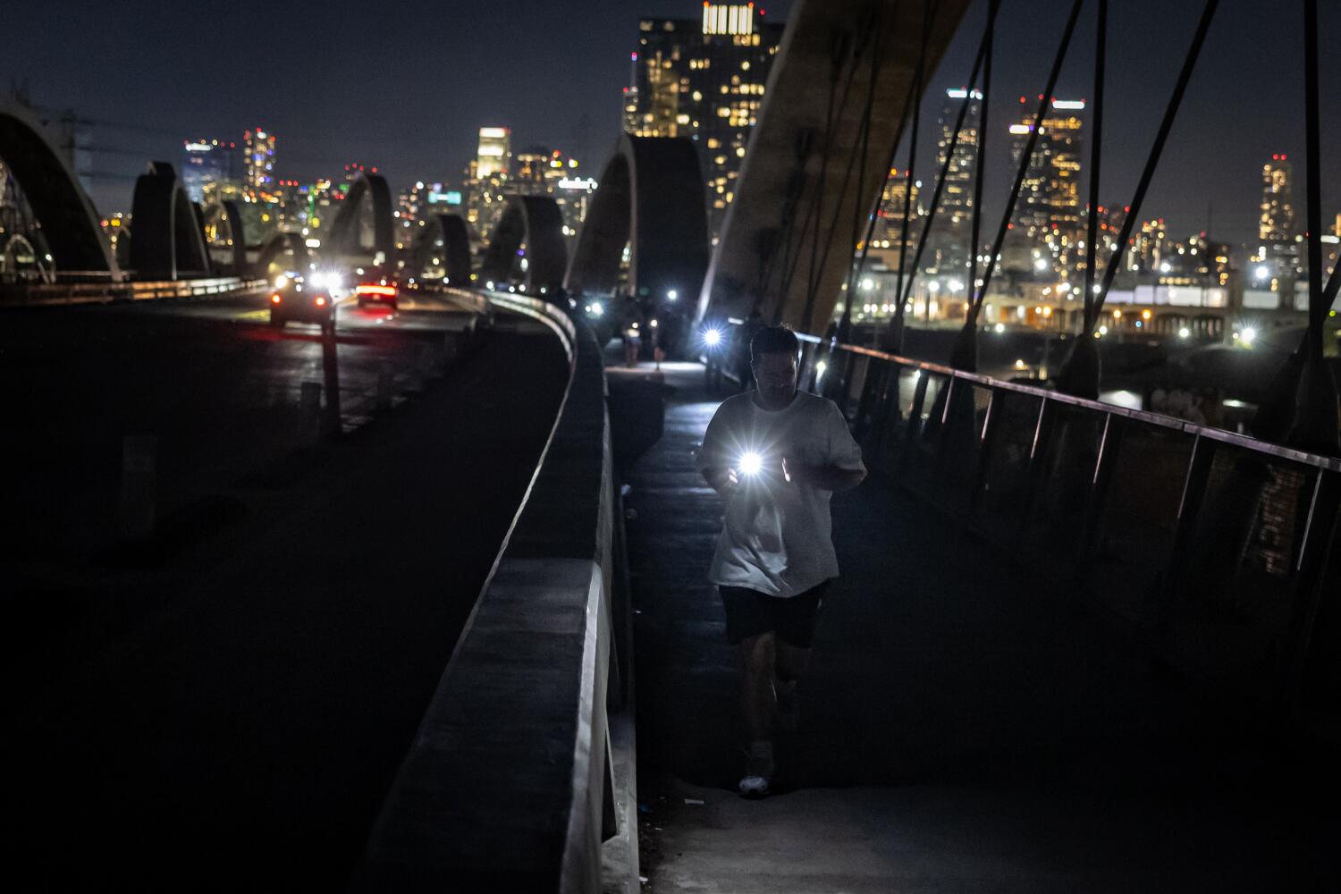 Los Angeles, CA - October 01: The Boyle Heights Bridge Runners running club run across the 6th street bridge which is unlit on Wednesday, Oct. 1, 2025 in Los Angeles, CA. (Jason Armond / Los Angeles Times)
