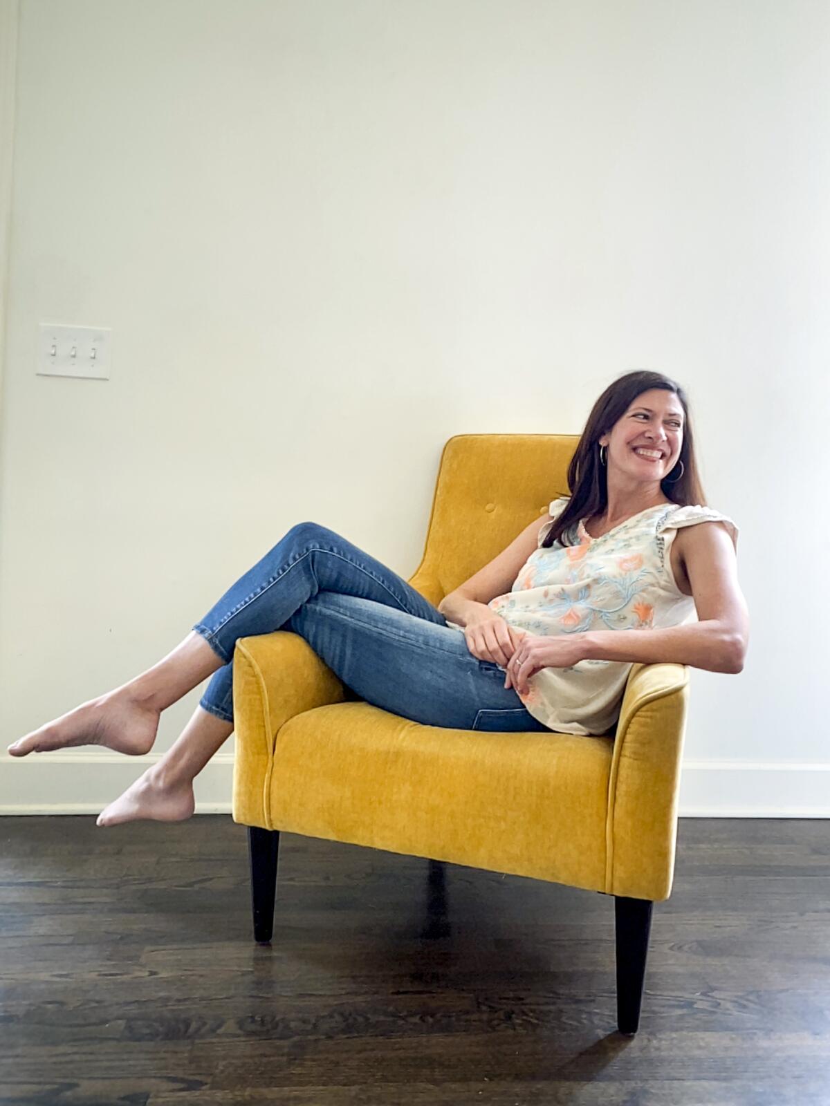 "Real World" star Julie Oliver in blue jeans and a floral top in a yellow chair, at her home outside Birmingham, Ala.