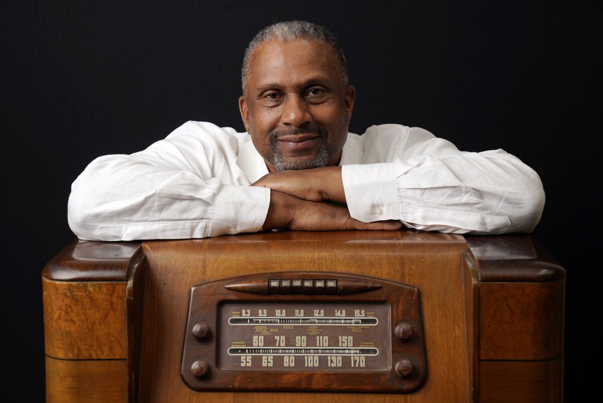 A man crosses his arms over an old-fashioned radio.