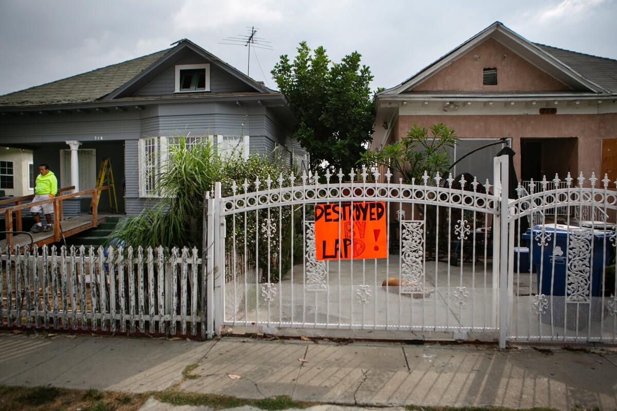 A man walks down a ramp outside a home next to a gate with a sign that says "Destroyed by LAPD"