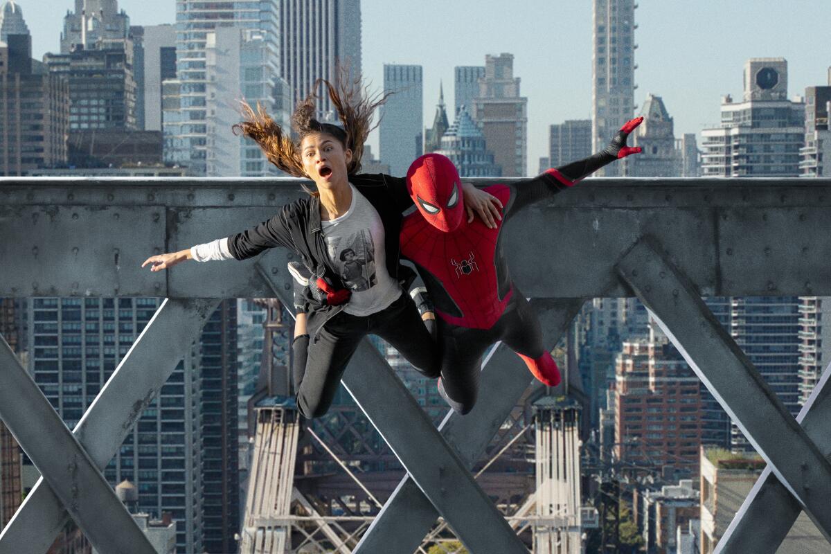 A woman and a man dressed as Spider-Man swing across a city skyline in a scene from "Spider-Man: No Way Home."