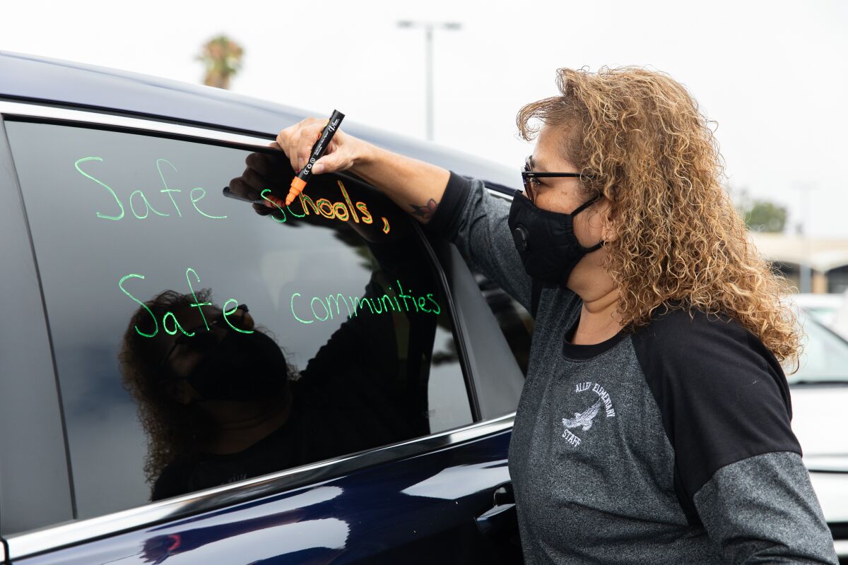 Gina-Marie McConkey writes “Safe schools, Safe communities” on a car window prior to a car caravan protest in Chula Vista.