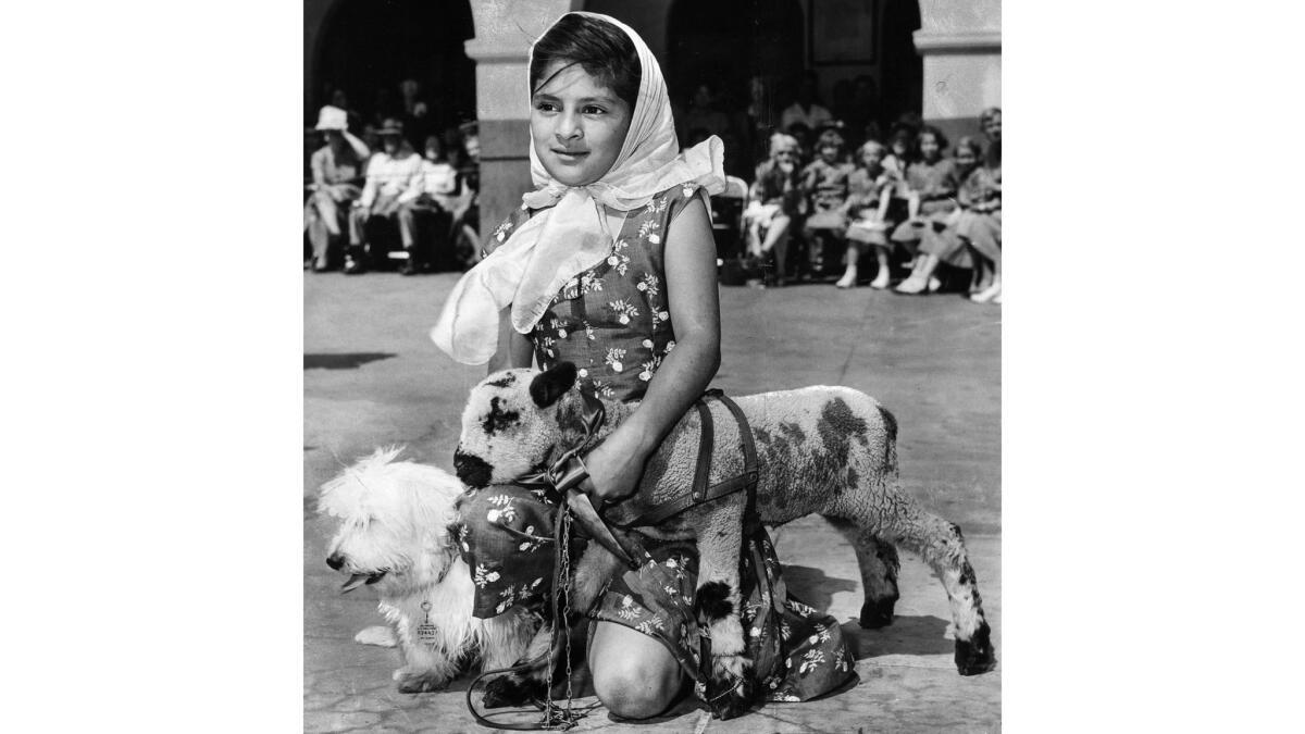 April 9, 1955: Virginia Peters, 9, kneels beside her pet lamb and dog in the courtyard of the Old Plaza Church where the pets receive an annual blessing.