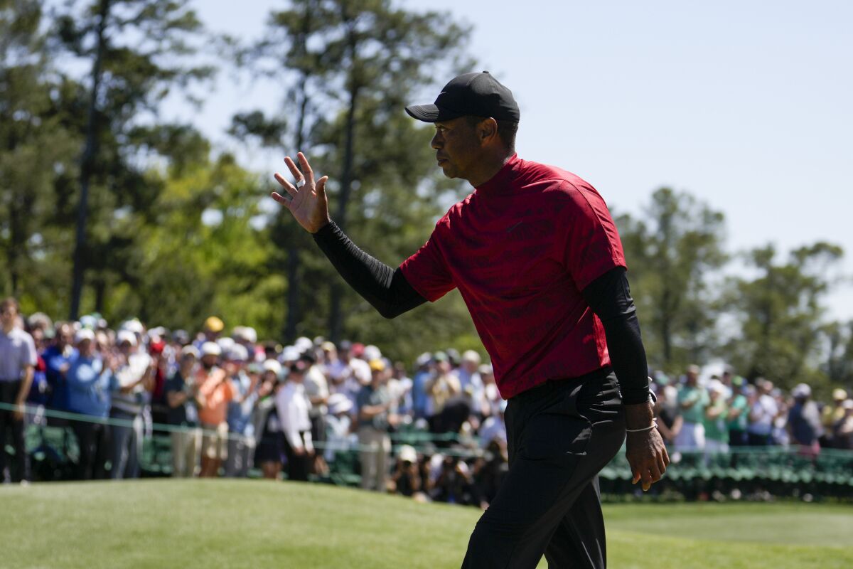 An unsmiling Tiger Woods, in his signature red shirt, waves to spectators at the Masters.