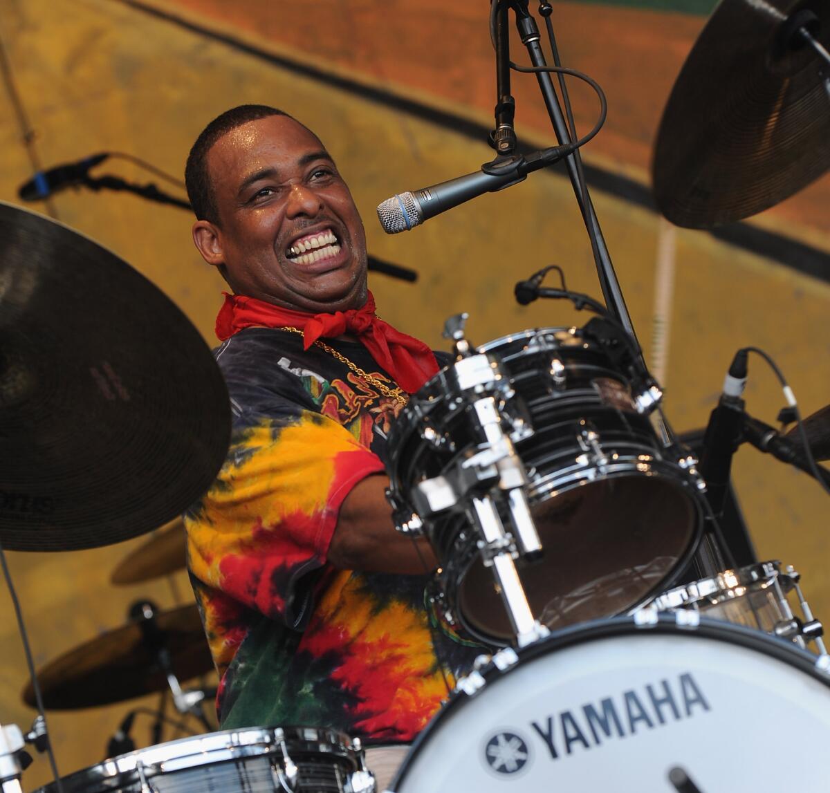 A smiling man performs behind a drum set at a festival.