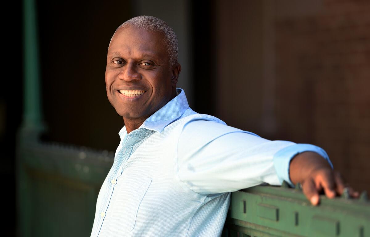 A smiling Andre Braugher stands, his arms outstretched and resting on the wall behind him