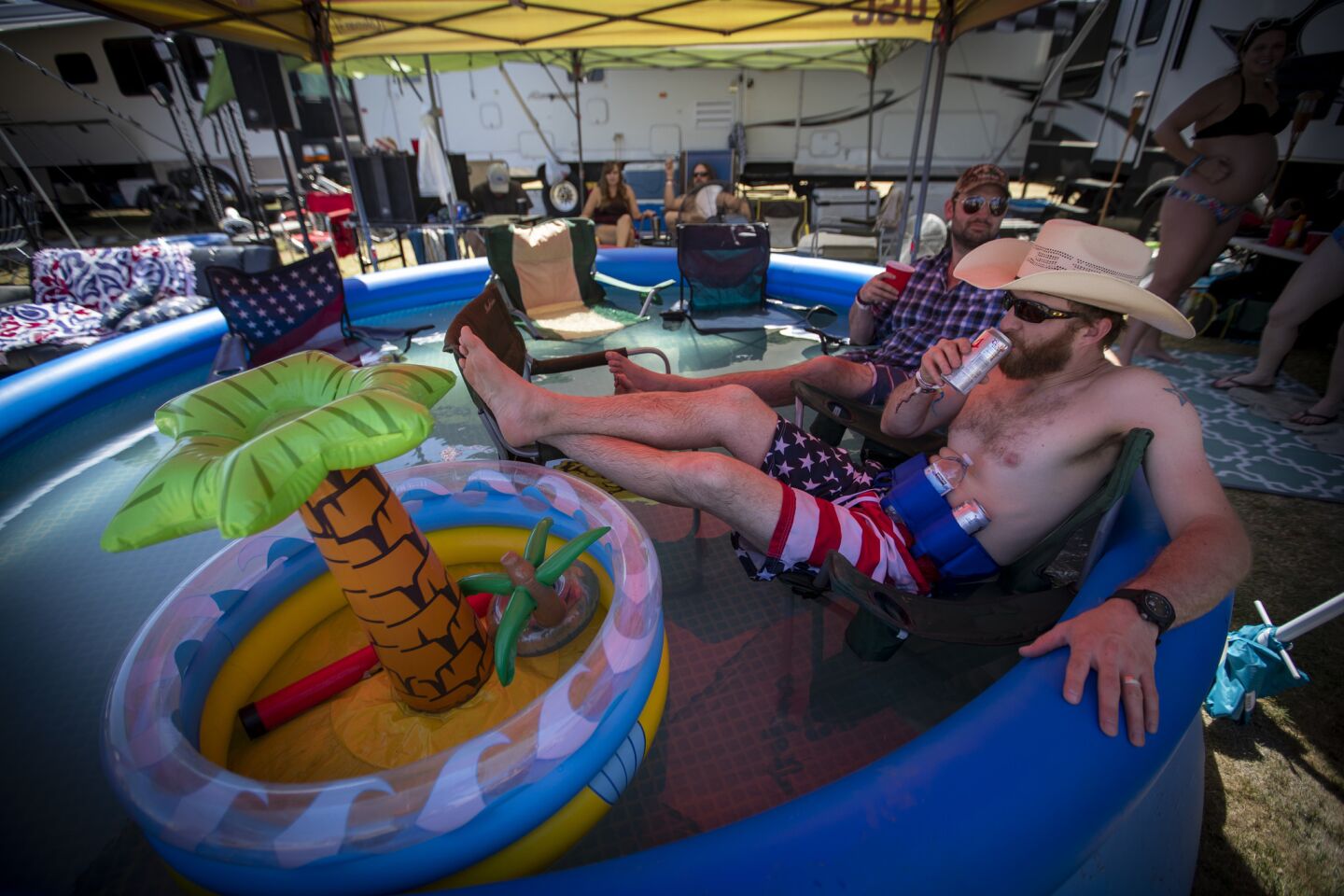 James, of Dallas, (no last name given) front, and John Rust of Portland, Ore., cool off in an inflatable swimming pool while listening to country music in the RV Resort area.