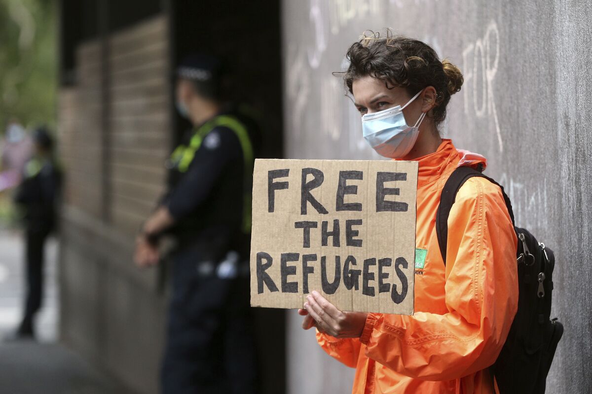 A protester holds a banner outside the Park Hotel calling for the release of refugees being detained inside the hotel in Melbourne, Australia, Saturday, Jan. 8, 2022. The world’s No. 1-ranked tennis player Novak Djokovic is also being held there after border officials canceled his visa last week over a vaccine requirement. (AP Photo/Hamish Blair)