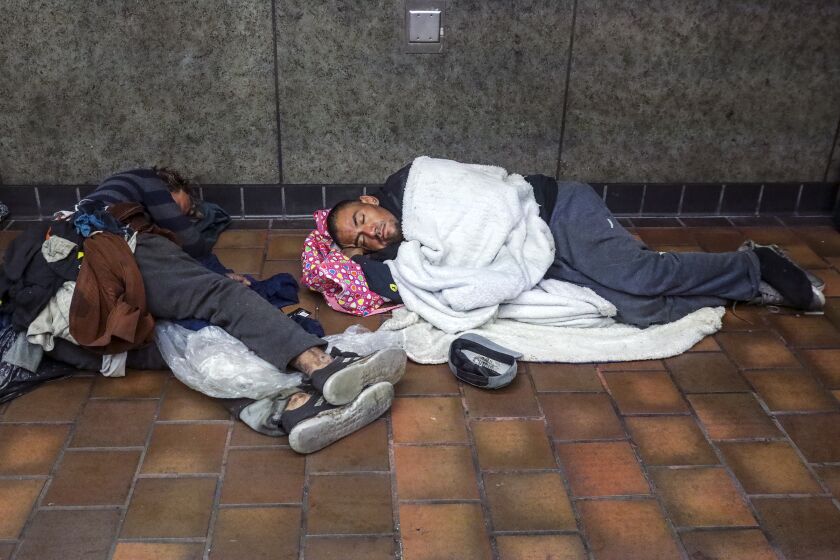 Los Angeles, CA - March 15: Homeless persons sleep in front of the closed gates of 7th. Street Metro station on Tuesday, March 15, 2022 in Los Angeles, CA. (Irfan Khan / Los Angeles Times)