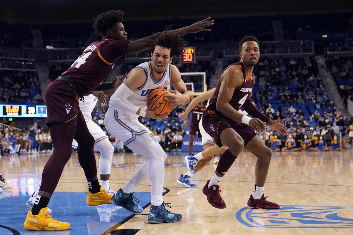 UCLA guard Jules Bernard grabs a rebound next to Arizona State center Enoch Boakye and forward Kimani Lawrence.