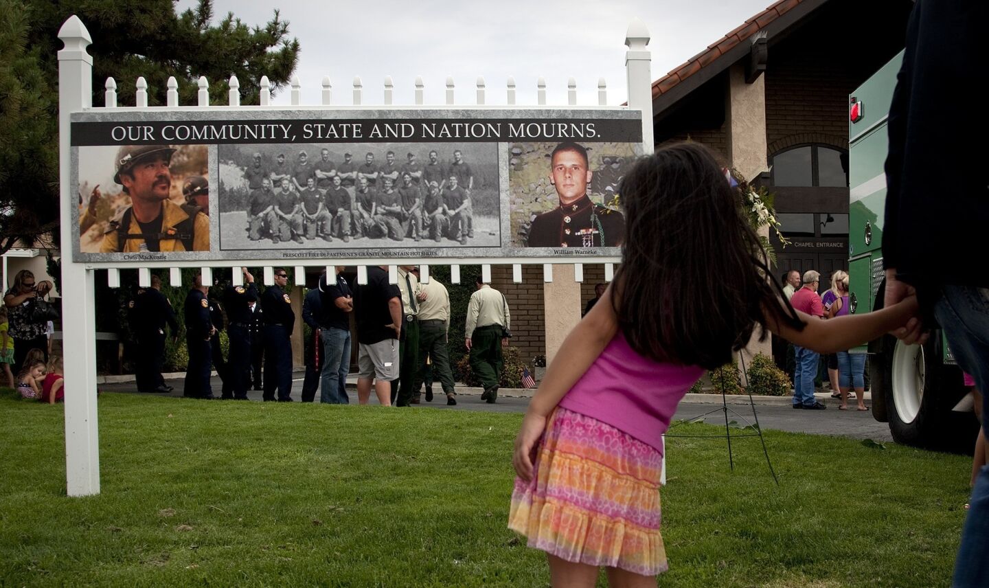 A girl looks at photos of fallen firefighters Christopher MacKenzie, left, and Kevin Woyjeck in Hemet. MacKenzie was from Hemet and Woyjeck grew up in Seal Beach.