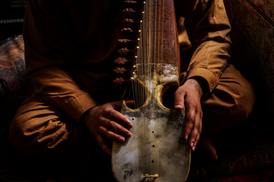 A man's hands are seen holding a rubab, a traditional Afghan stringed instrument