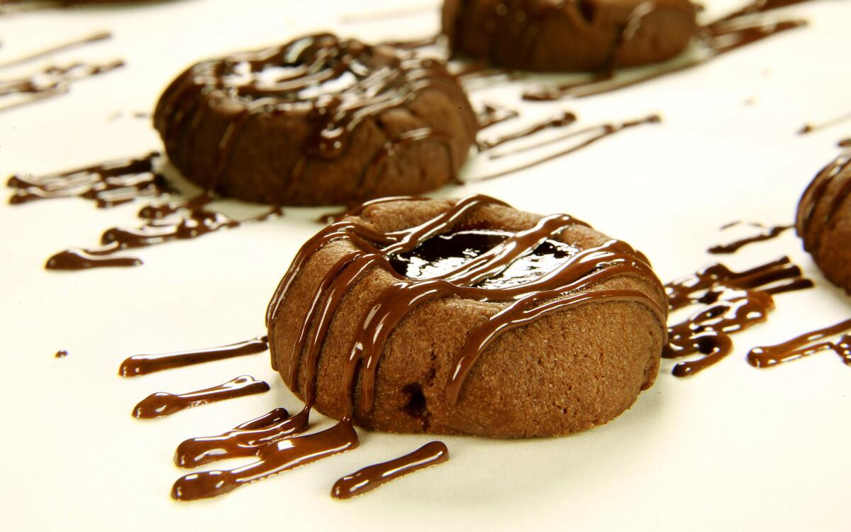 Chocolate-raspberry thumbprint cookies freshly drizzled with melted chocolate, ready to be placed on a serving dish.