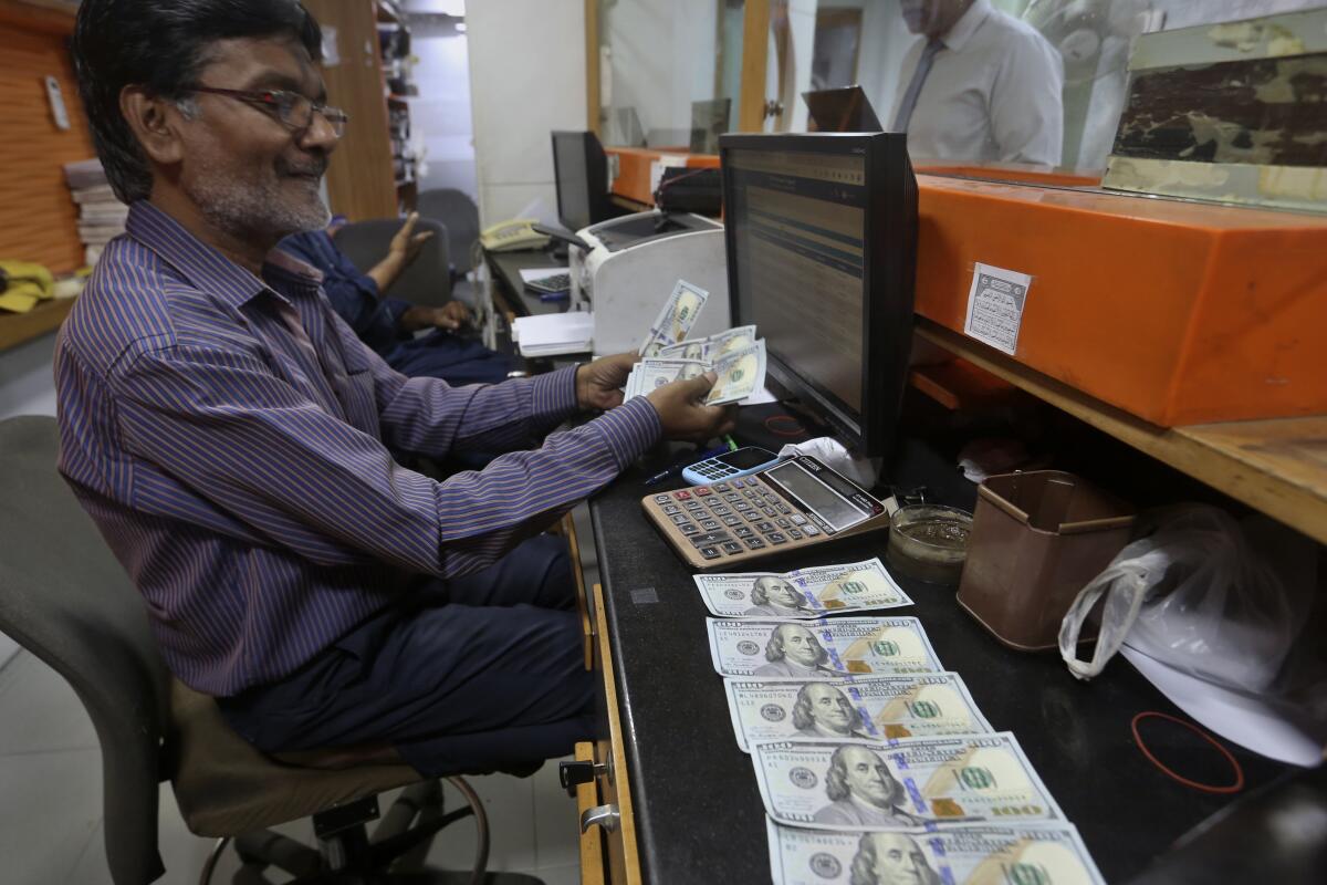 A Pakistani money trader counts U.S. dollars for a customer at a currency exchange office, in Karachi, Pakistan, Thursday, May 19, 2022. Pakistan’s currency has plummeted to an all-time record low in intraday trading against the U.S. dollar amid uncertainty about the success of crucial talks between the International Monetary Fund and the government of Prime Minister Shahbaz Sharif, which is considering massive new taxation to avoid a default. (AP Photo/Fareed Khan)