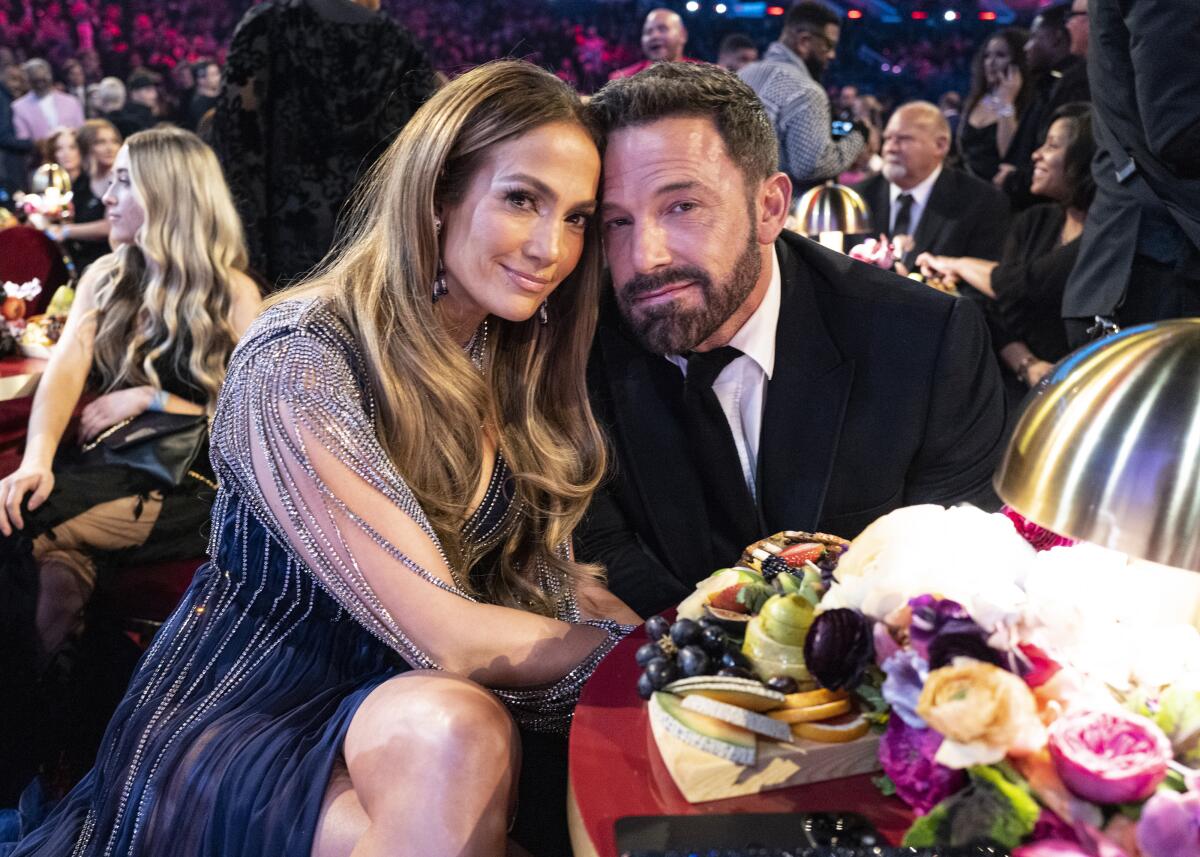 Jennifer Lopez and Ben Affleck lean their heads together while sitting at a table with flowers on it