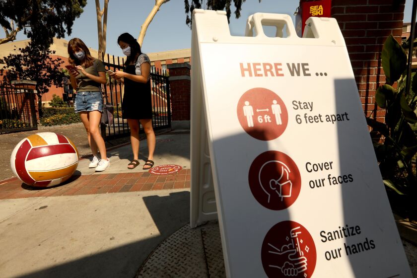 LOS ANGELES, CA - AUGUST 17, 2020 - - USC students Madeline Aguirre, 19, left, and Megan Tran, 20, do their wellness screening to enter campus online while standing next to a sign that shows three steps to keep the coronavirus at bay on the first day of academic instruction on the USC campus in Los Angeles on August 17, 2020. (Genaro Molina / Los Angeles Times)