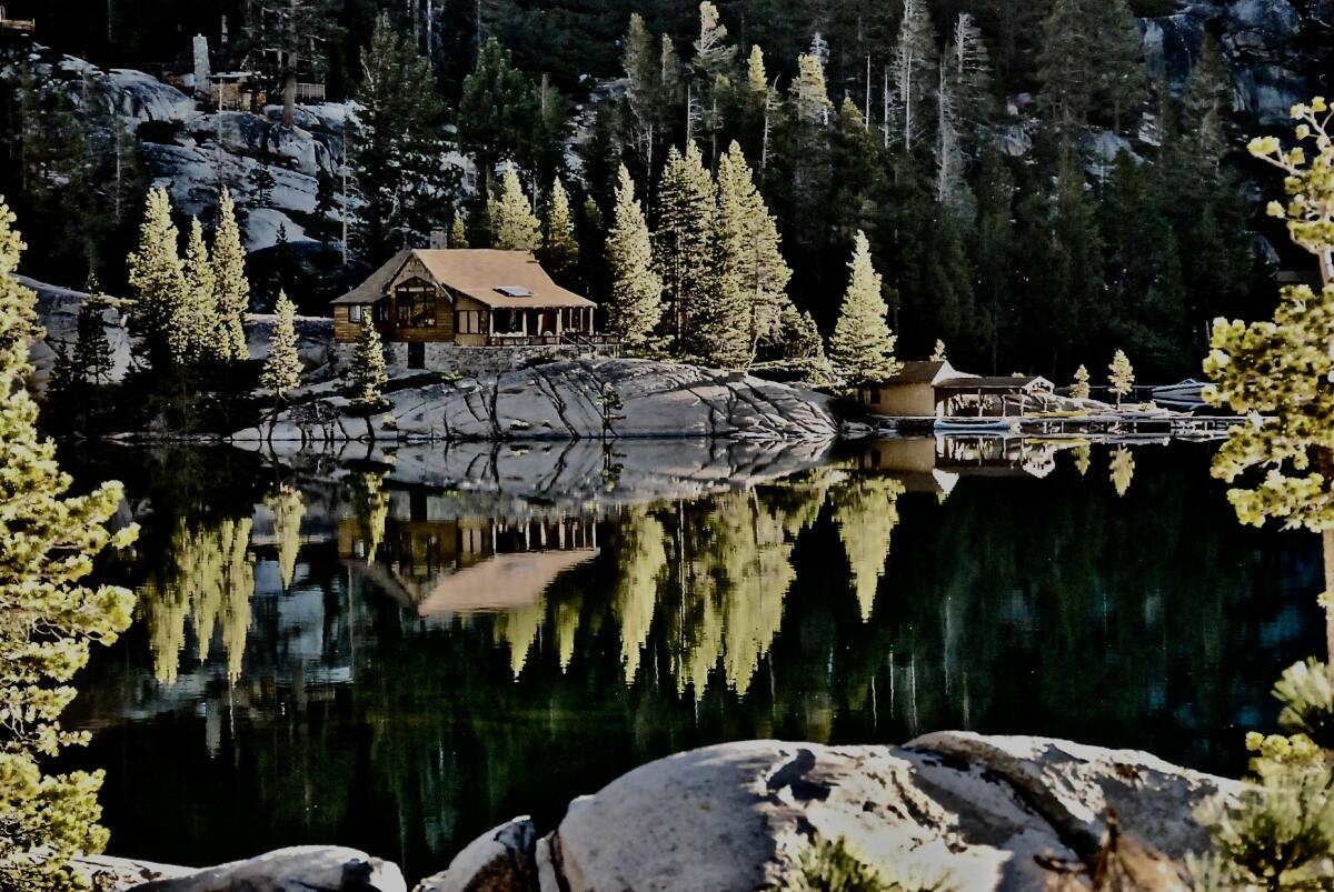 A cabin surrounded by trees is reflected in a lake.