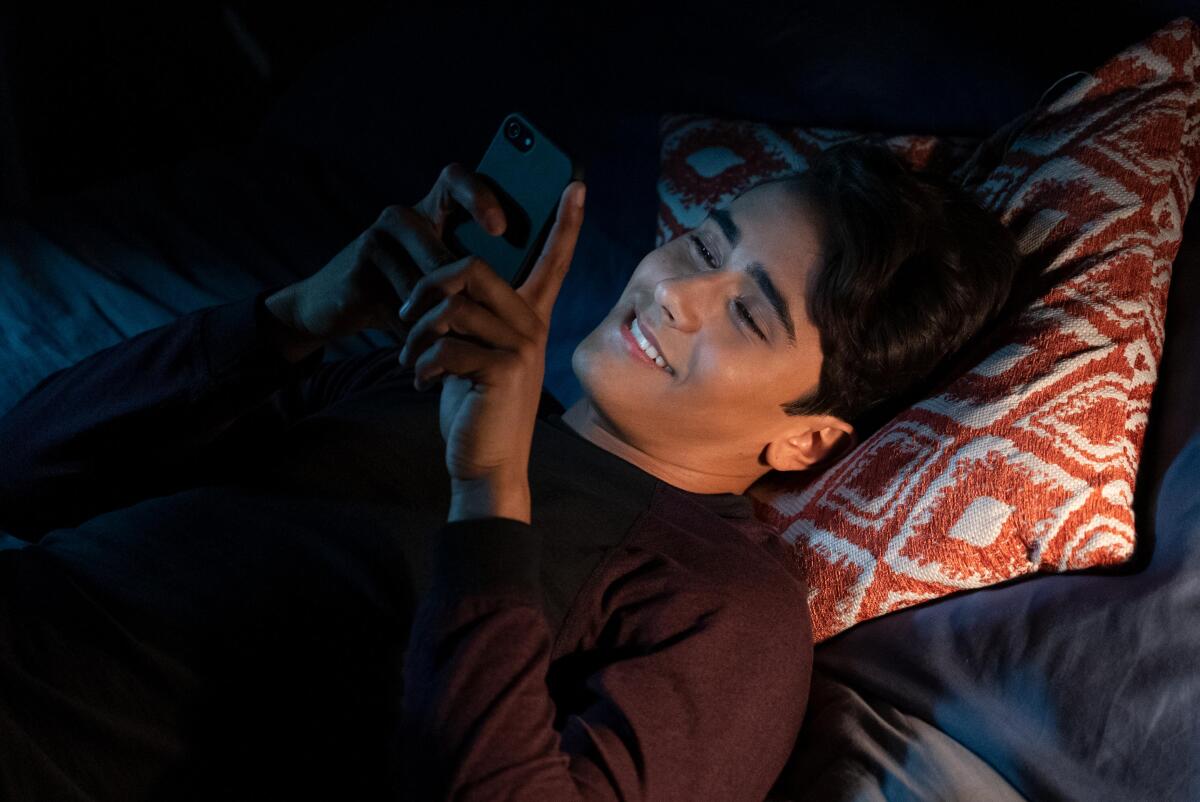A teenage boy laying in bed texting and smiling