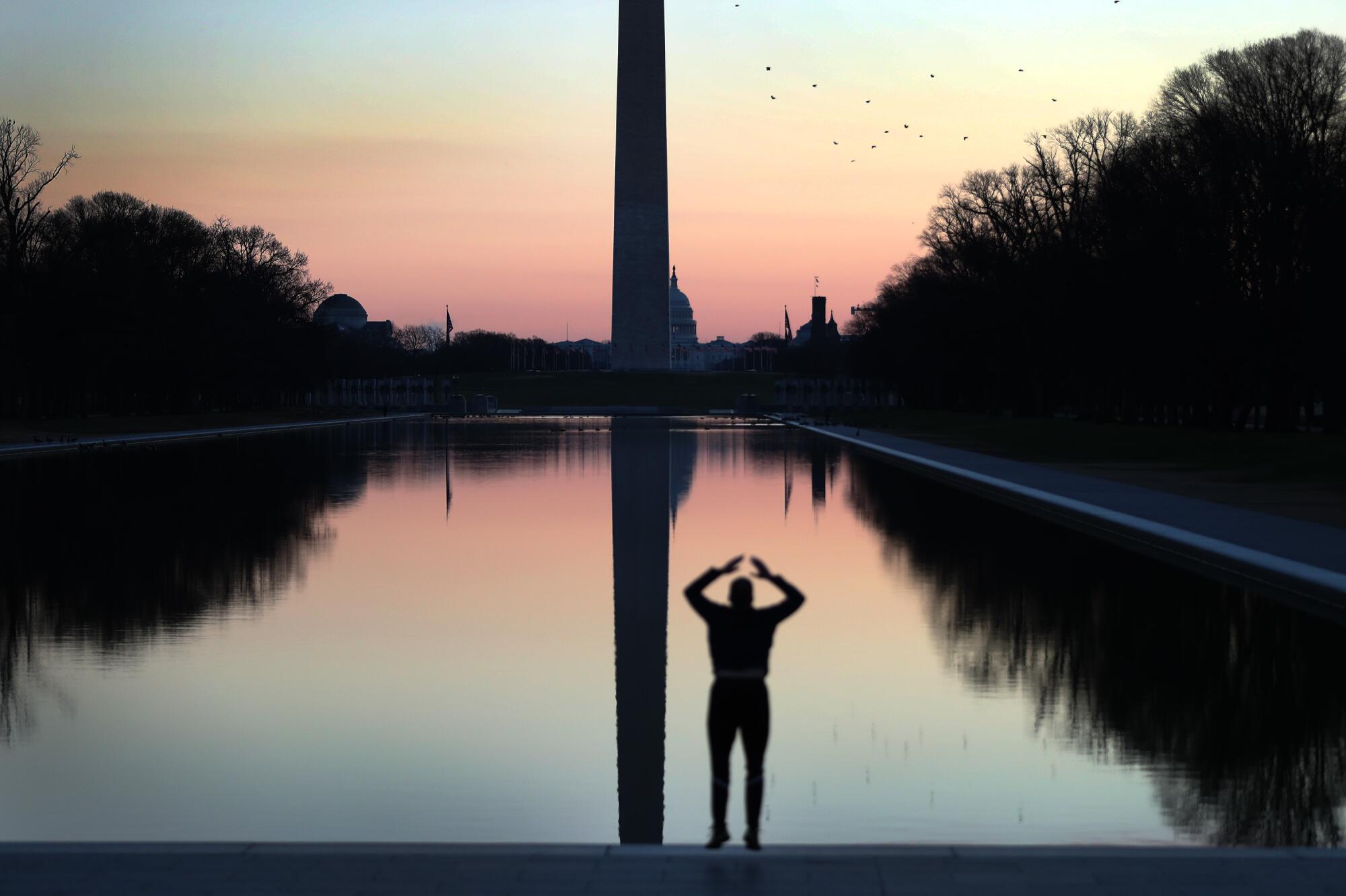 A person exercises by the Reflecting Pool, with the U.S. Capitol visible behind the Washington Monument.