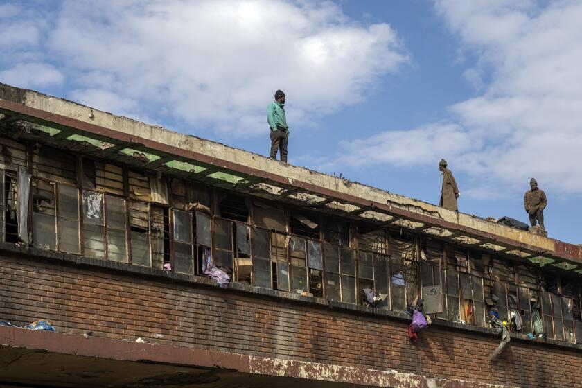 Squatters stand on a rooftop overlooking the scene of one of South Africa's deadliest inner-city fires in Johannesburg, South Africa, Friday, Sept. 1, 2023. Emergency services teams have left the scene of one of South Africa's deadliest inner-city fires as pathologists faced the grisly task Friday of identifying dozens of charred bodies and some separate body parts that had been transported to several mortuaries across the city of Johannesburg. (AP Photo/Jerome Delay)