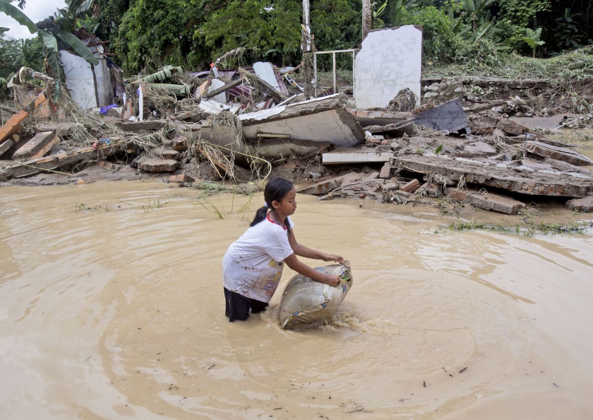 A young girl washes a pillow in flood water near ruins of houses at a neighborhood affected by the flood in Medan, North Sumatra, Indonesia, Friday, Dec. 4, 2020. Torrential rains in the country's third largest city swelled rivers and flooded thousands of homes leaving a number of people killed and missing. (AP Photo/Binsar Bakkara)