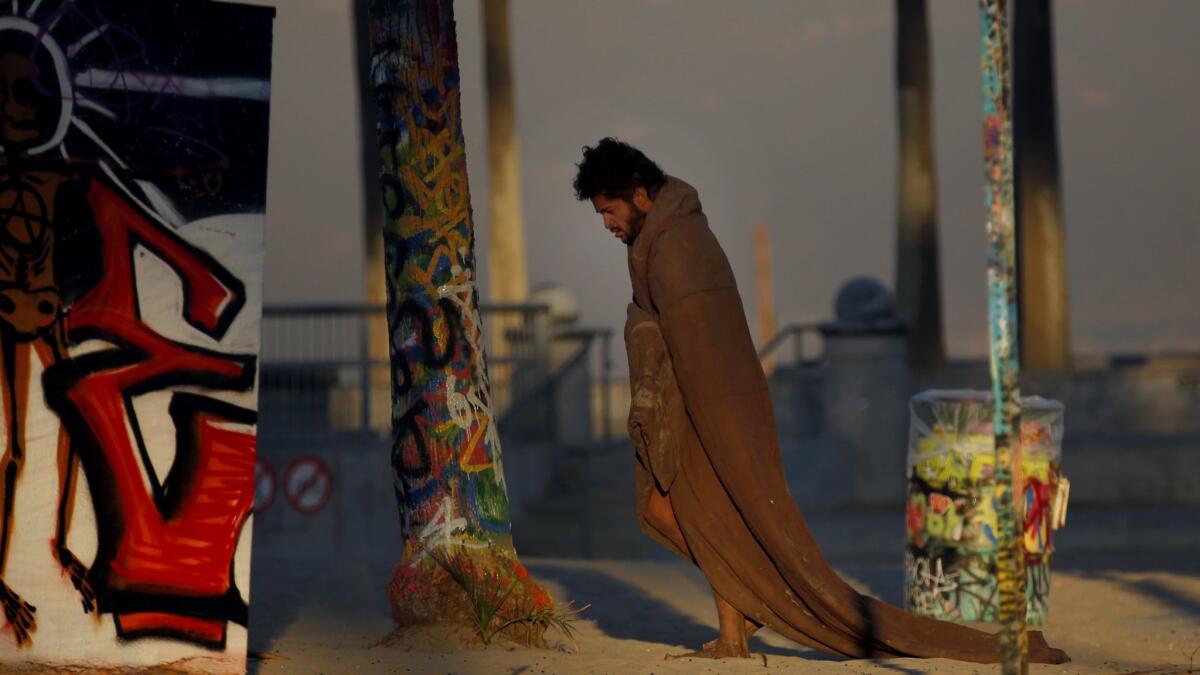 A homeless man walks around Venice Beach wearing a blanket.