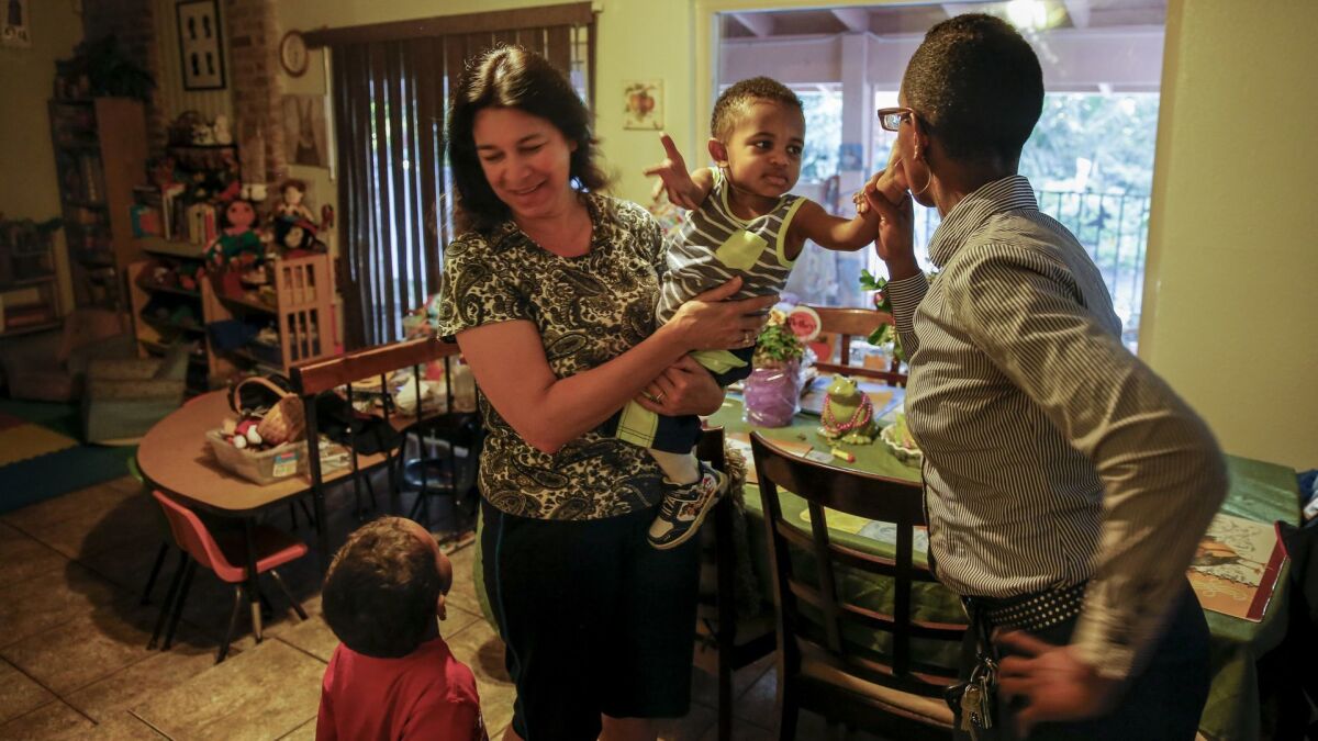 Francis Brown, 37, right, kisses her son Samson goodbye while her other son, Samuel, tries to get the attention of Virginia Perez, the family's child-care provider, in 2017.